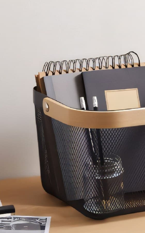 Black mesh storage basket with a wooden handle holding notebooks on a desk